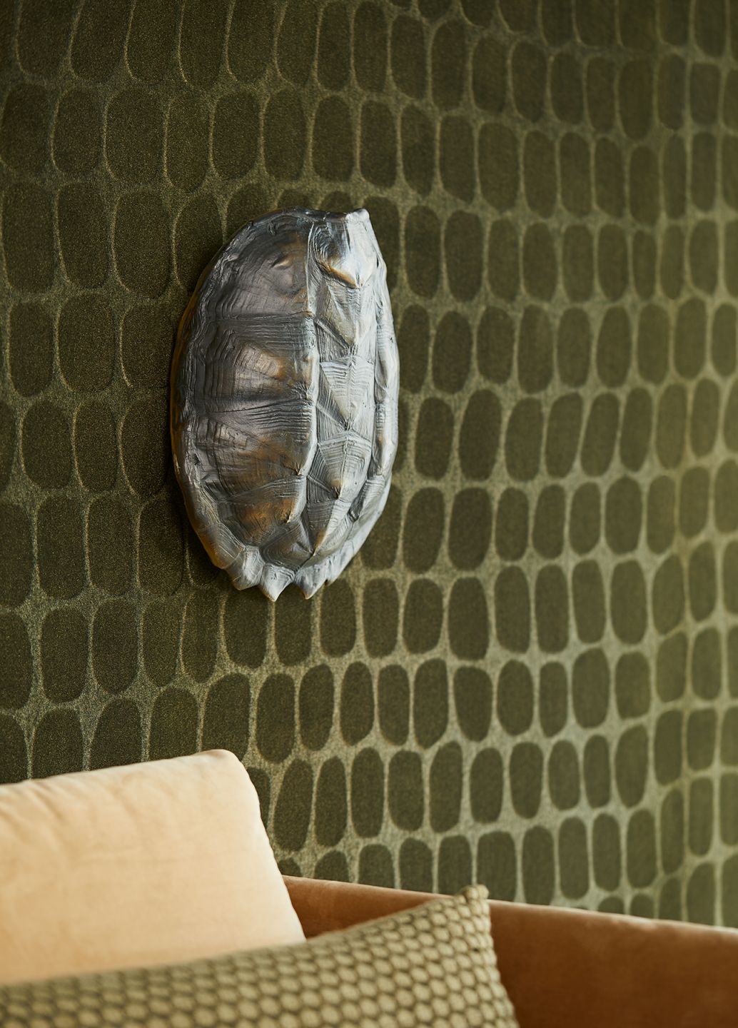A dark green flock wallpaper with a large-scale crocodile-skin pattern and tactile relief, with a beige armchair in front of it