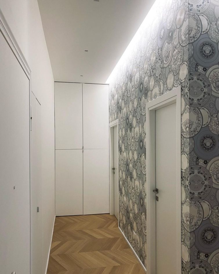 Papel de parede cinzento com desenho inspirado nas placas de Versace, aplicado numa parede de um corredor com duas portas