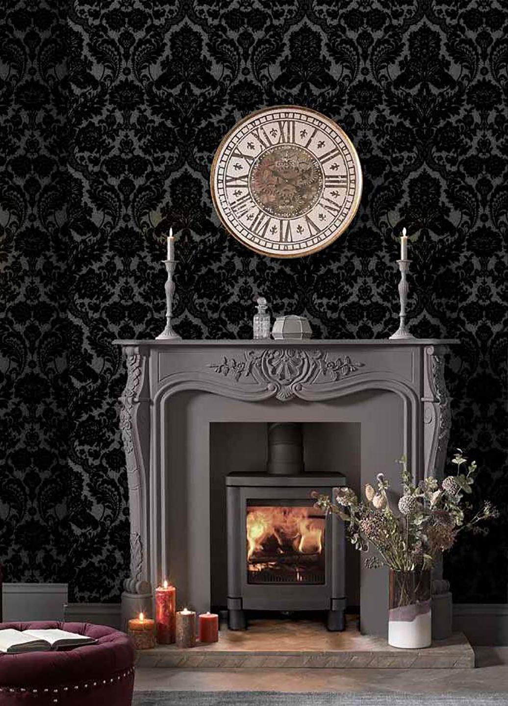 A black damask wallpaper with thick flock relief around a grey fireplace with a fire burning in it