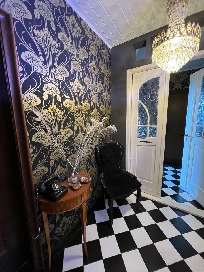 Un corridoio con una porta, sulla parete una carta da parati nera con motivi art nouveau dorati