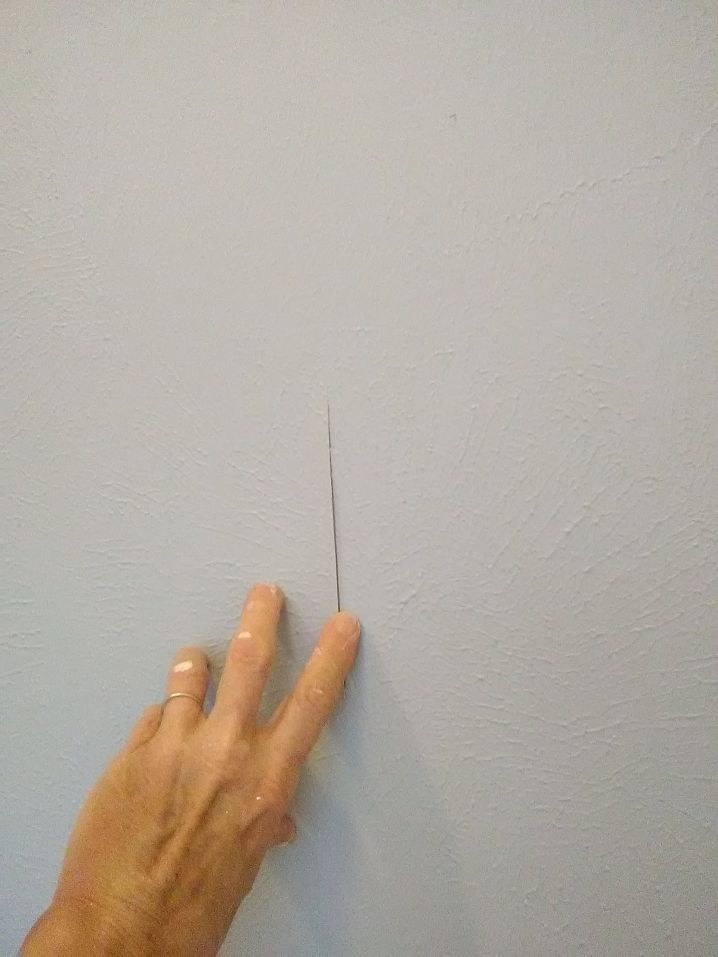 Close-up of a hand pointing to a thin crack on a painted wall surface