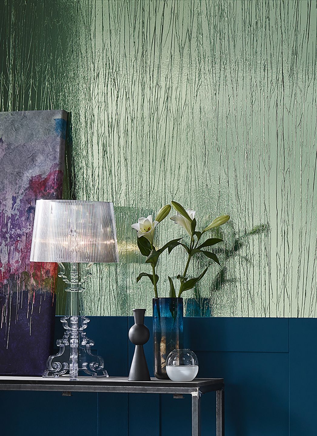 A shiny green crinkle-look metallic crush wallpaper behind a side table with a lamp and a flower vase