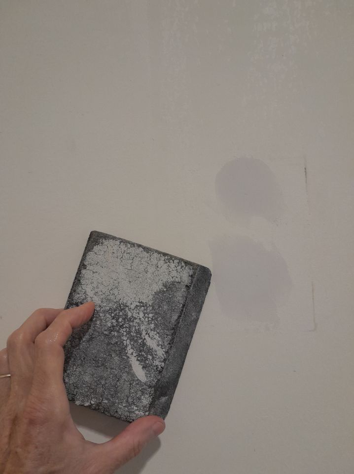Hand sanding down wall imperfections before wallpapering