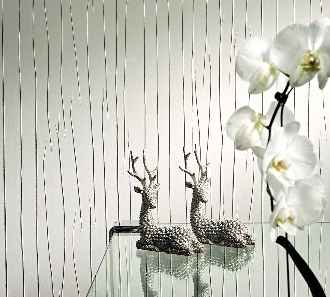 Papel de parede de cor creme e aparência enrugada por trás de uma mesa de apoio de vidro com uma orquídea e duas estatuetas decorativas em forma de veado