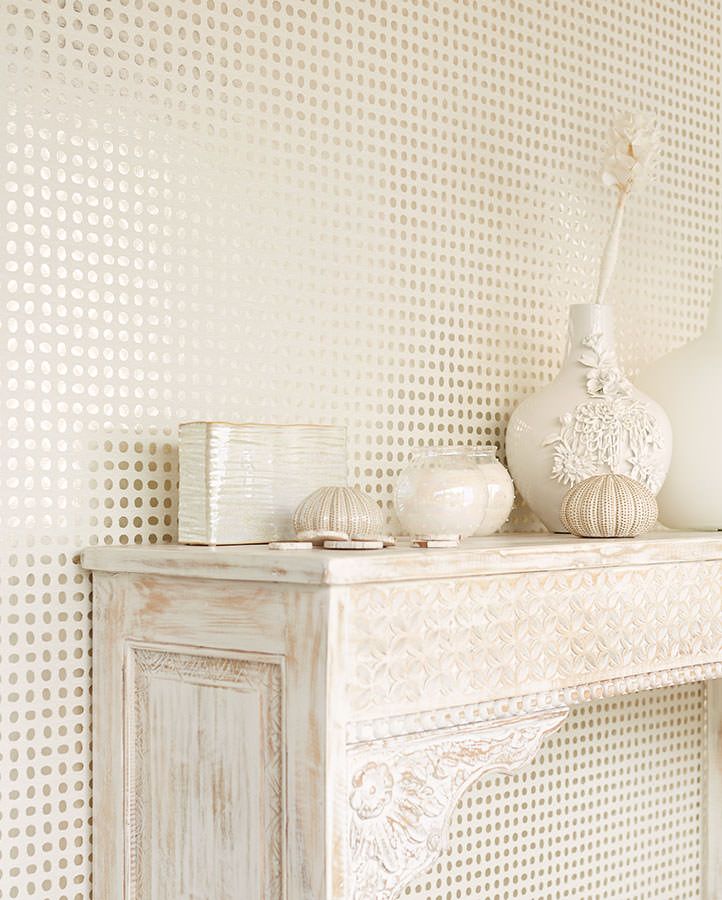 A cream-coloured wallpaper with many small shiny golden dots on the wall behind a shelf with vases