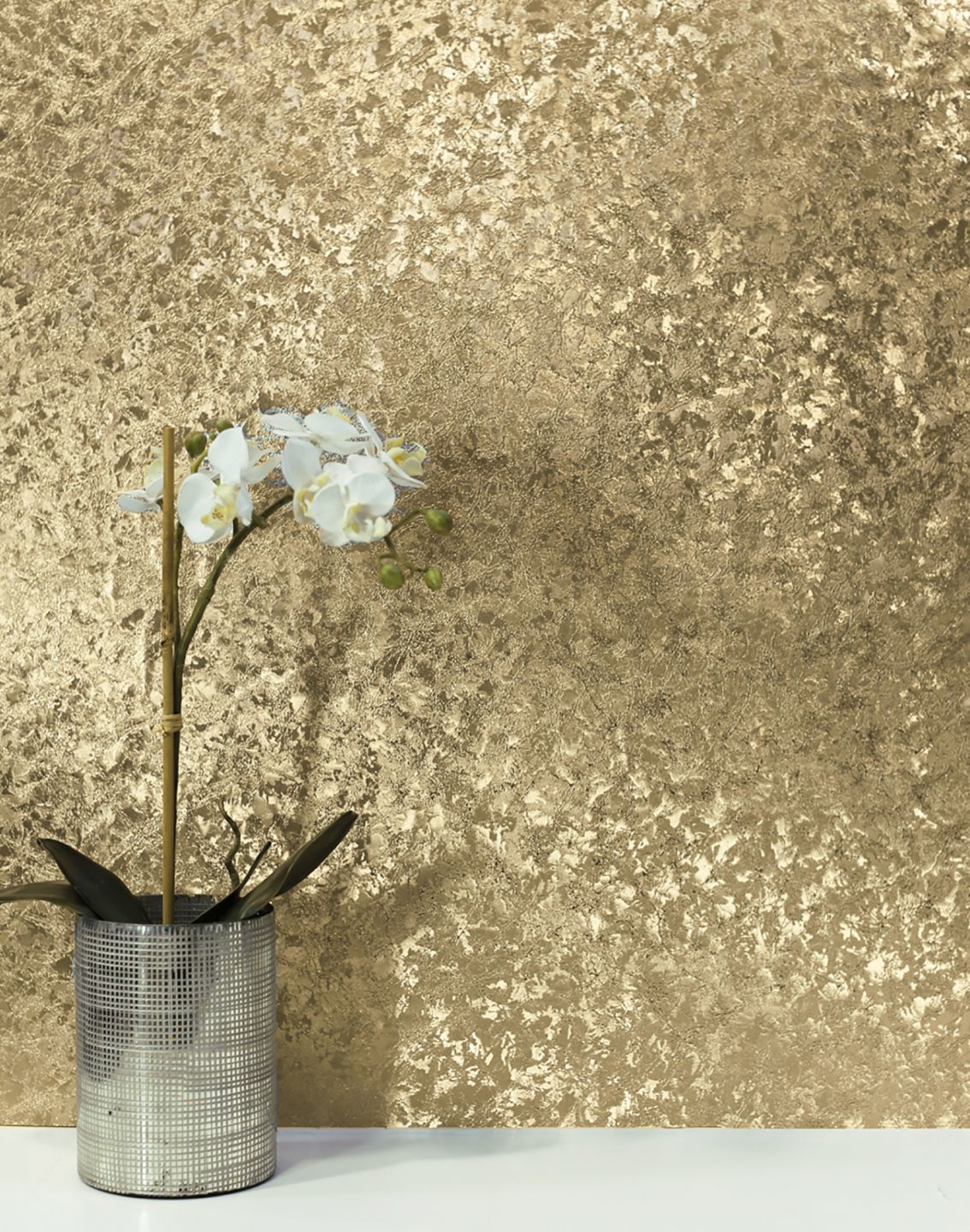A shiny gold-coloured metal wallpaper on the wall behind a vase with a white orchid