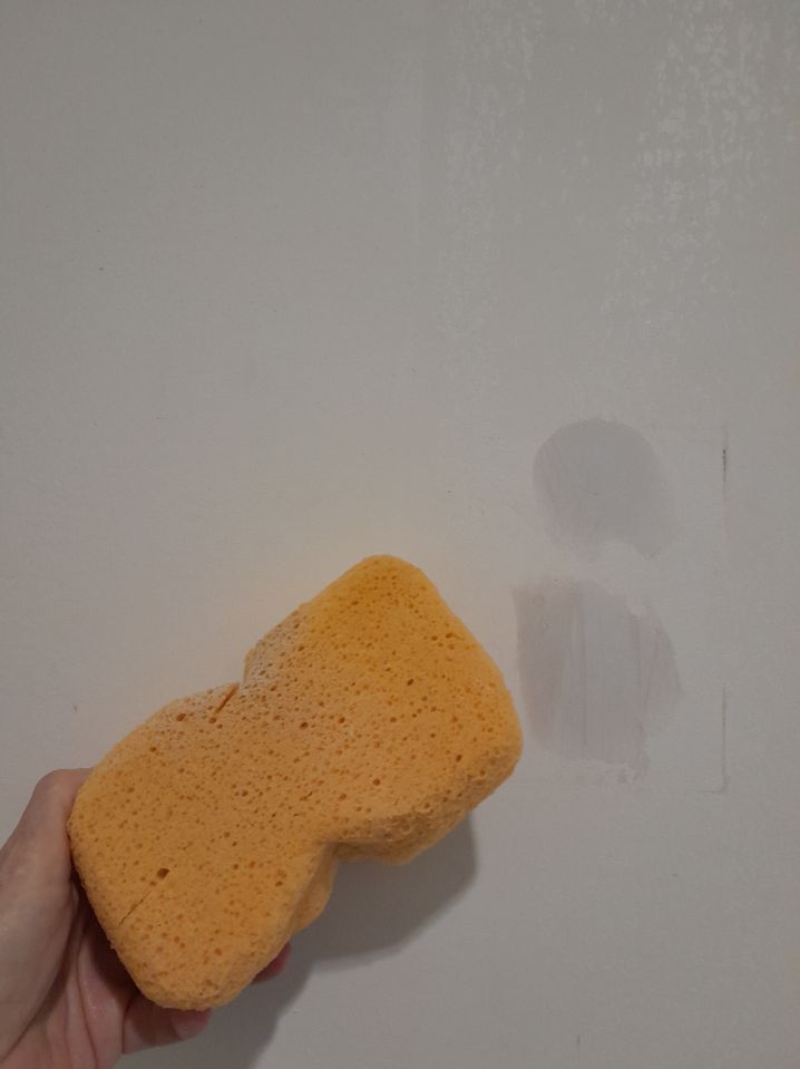 Mano limpiando una pared con esponja húmeda antes de empapelar